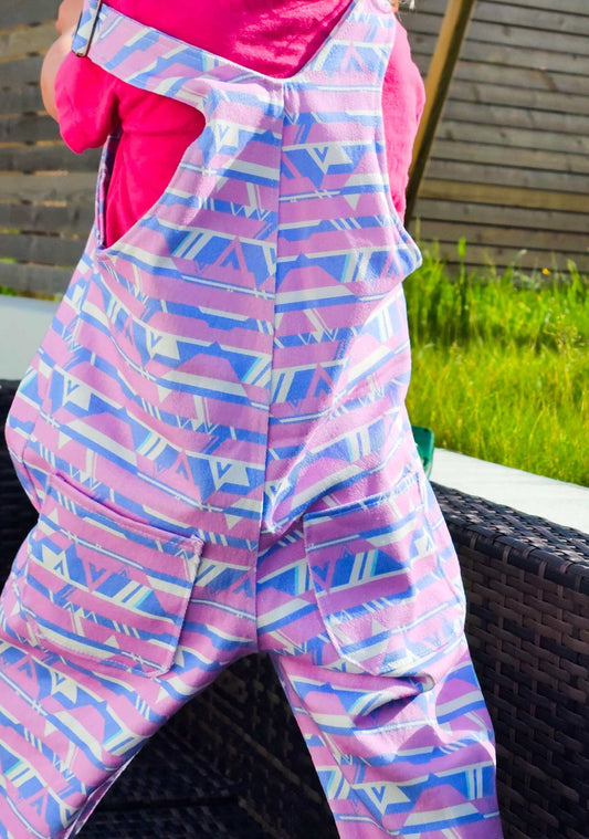 Child wearing colorful patterned dungarees with adjustable straps and pockets outdoors